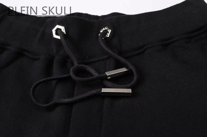 Close-up of black sweatpants with a black drawstring and silver metal accents, featuring the text 'PLEIN SKULL' in the top left corner.