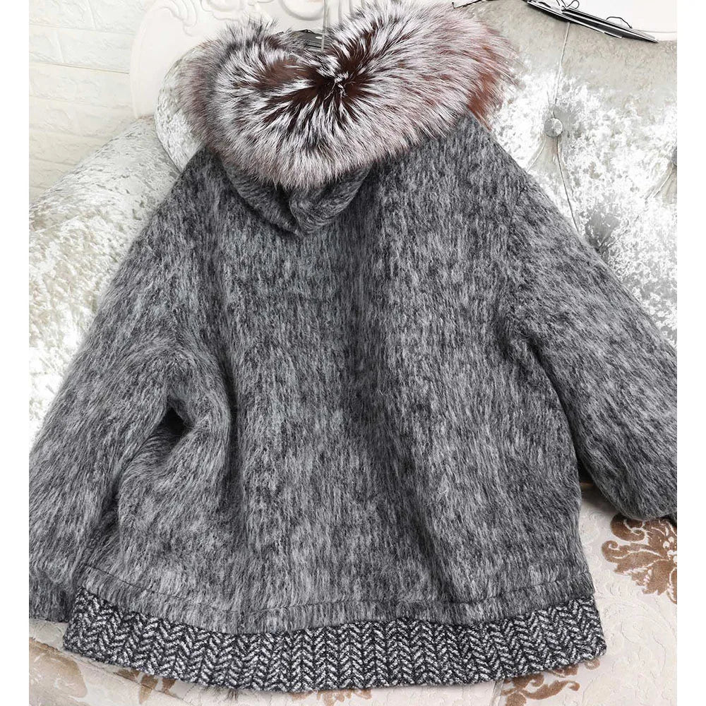 A gray marled knit hooded jacket with a large brown and white faux fur hood trim and a patterned knit hem, displayed on a tufted white sofa.