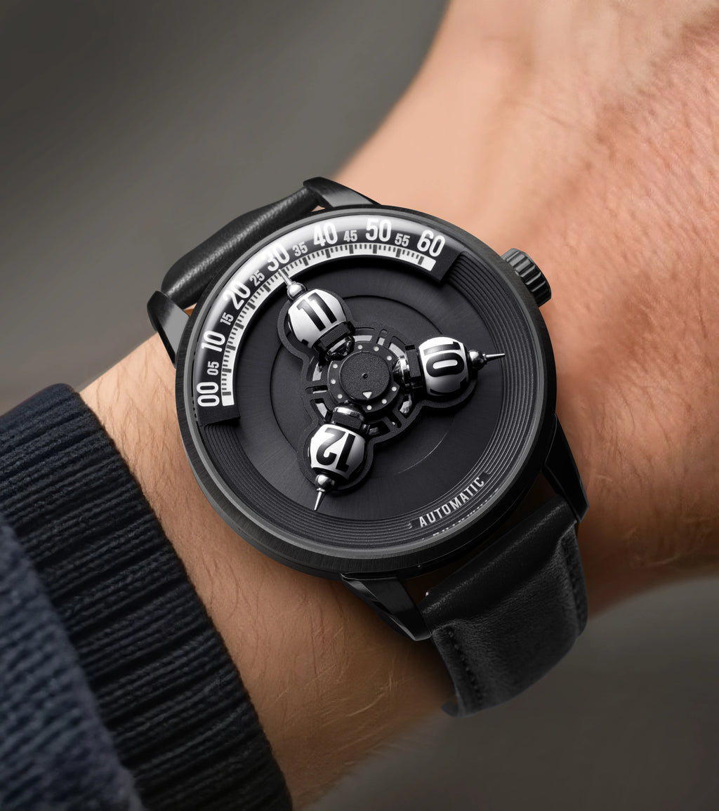 A close-up of a wrist wearing a black dial watch with a skeletonized face, silver-toned hands and markers, and a black leather strap.