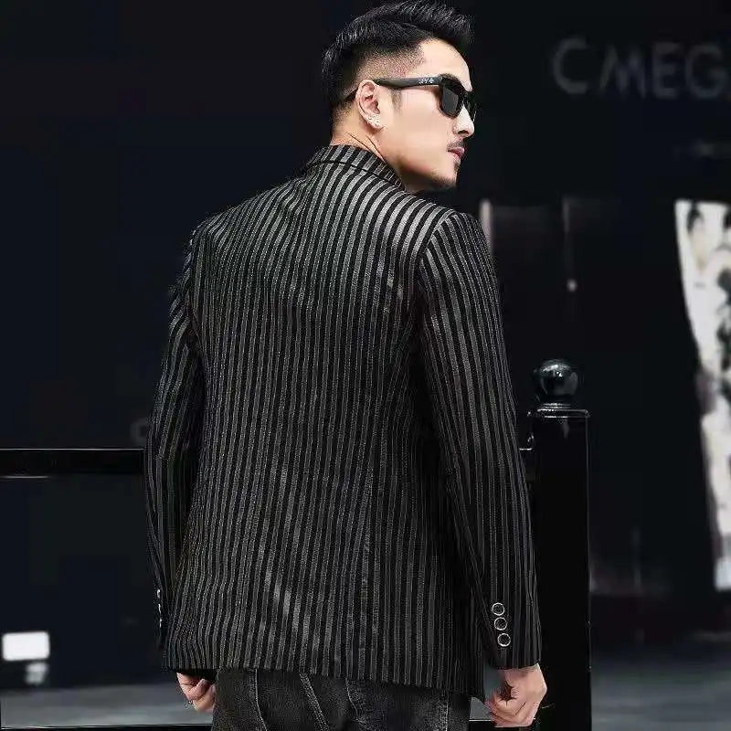 A man wearing a black and gray vertically striped blazer and dark sunglasses, photographed from the back in a dark indoor setting.