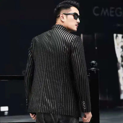 A man wearing a black and gray vertically striped blazer and dark sunglasses, photographed from the back in a dark indoor setting.