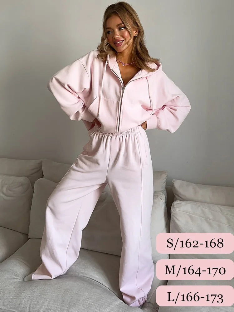 Woman wearing a pink tracksuit standing on a couch with size information displayed.