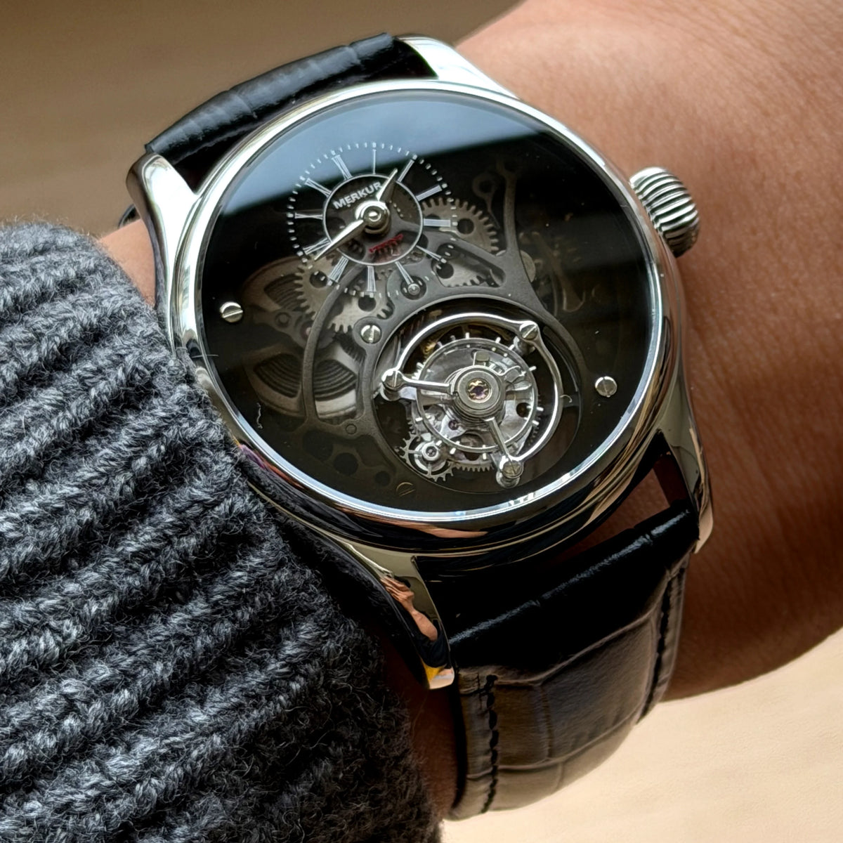 Close-up of a person wearing a black wristwatch with a visible mechanical movement.