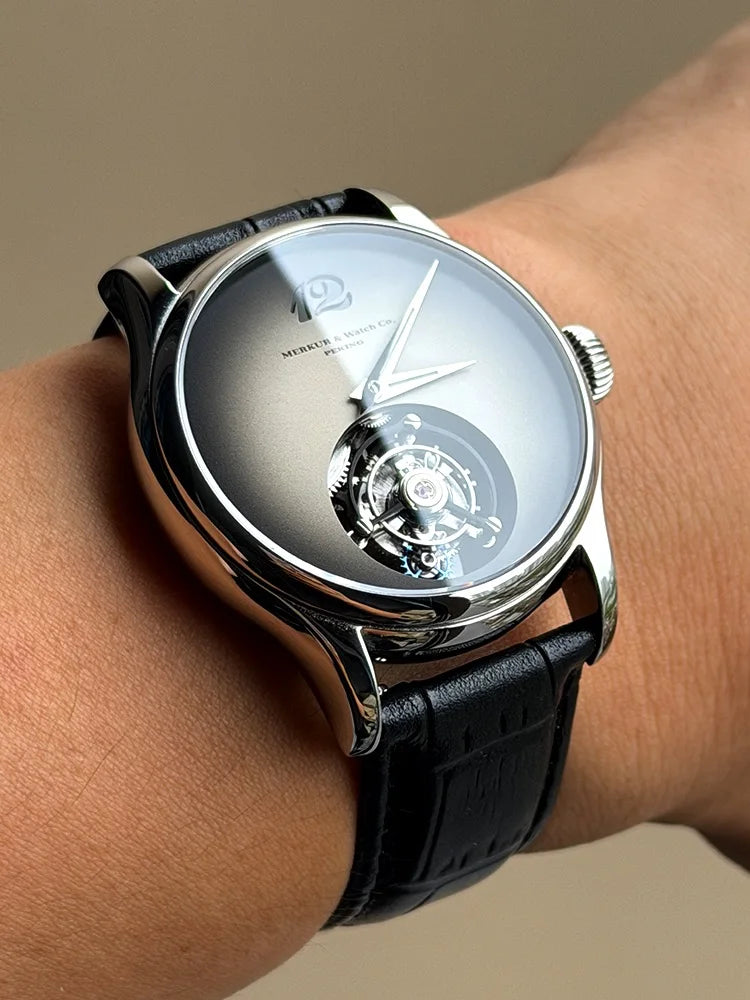 Luxury watch with black leather strap on a wrist against a neutral background