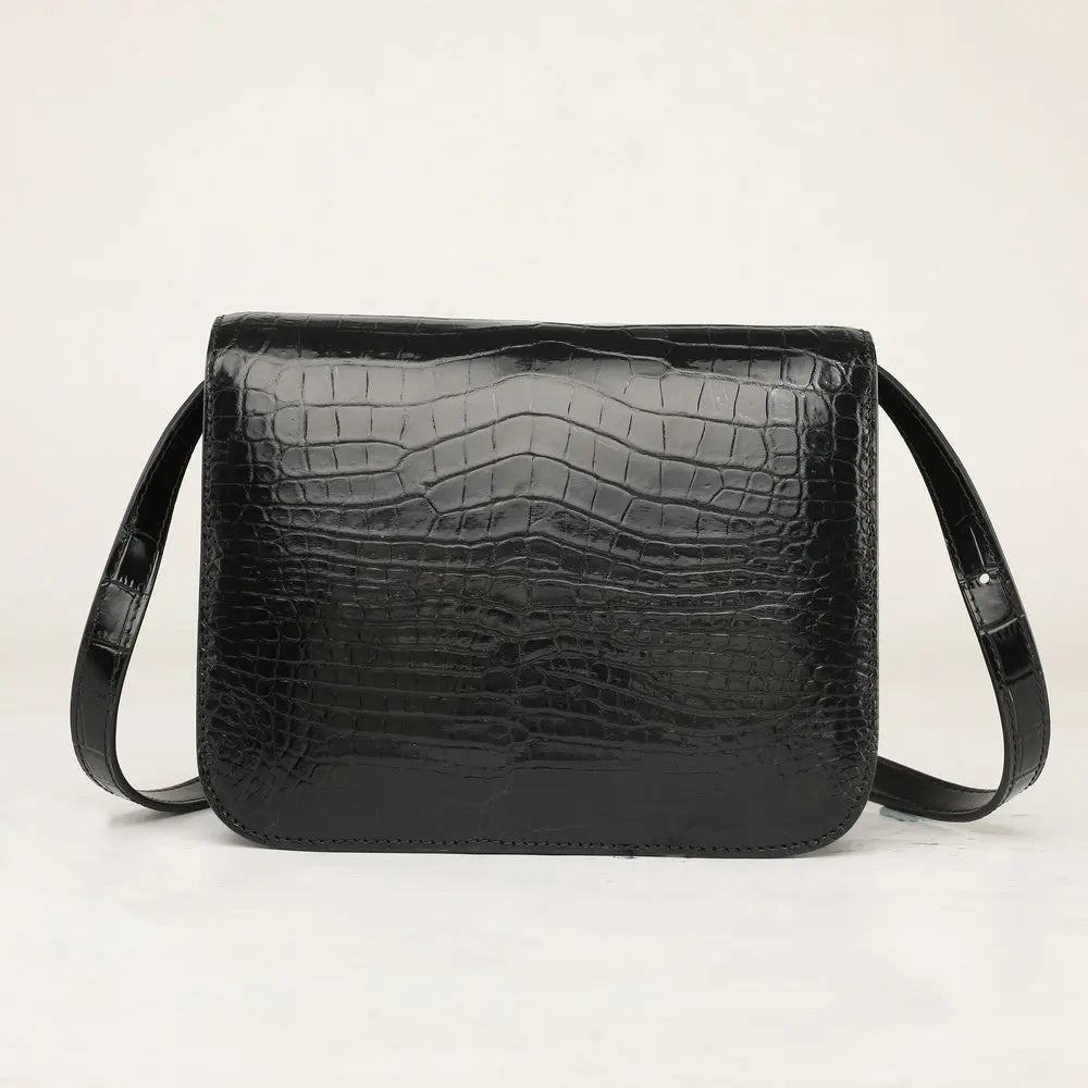 A black crocodile-embossed leather shoulder bag with a rectangular shape and a single strap, photographed against a plain off-white background.
