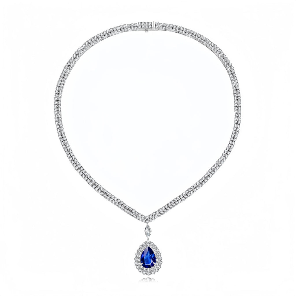 A silver-tone necklace featuring a textured chain paved with small clear stones, with a teardrop-shaped blue gemstone pendant surrounded by a halo of clear stones, shown on a white background.