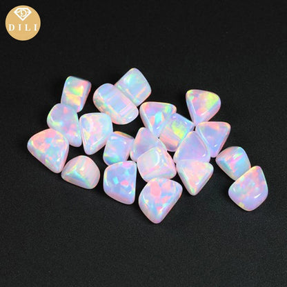 A pile of small, polished tumbled opal stones with a pearlescent white body and vibrant iridescent rainbow flashes, displayed on a solid black background. A gold circular logo for 'DILI' is visible in the top-left corner.