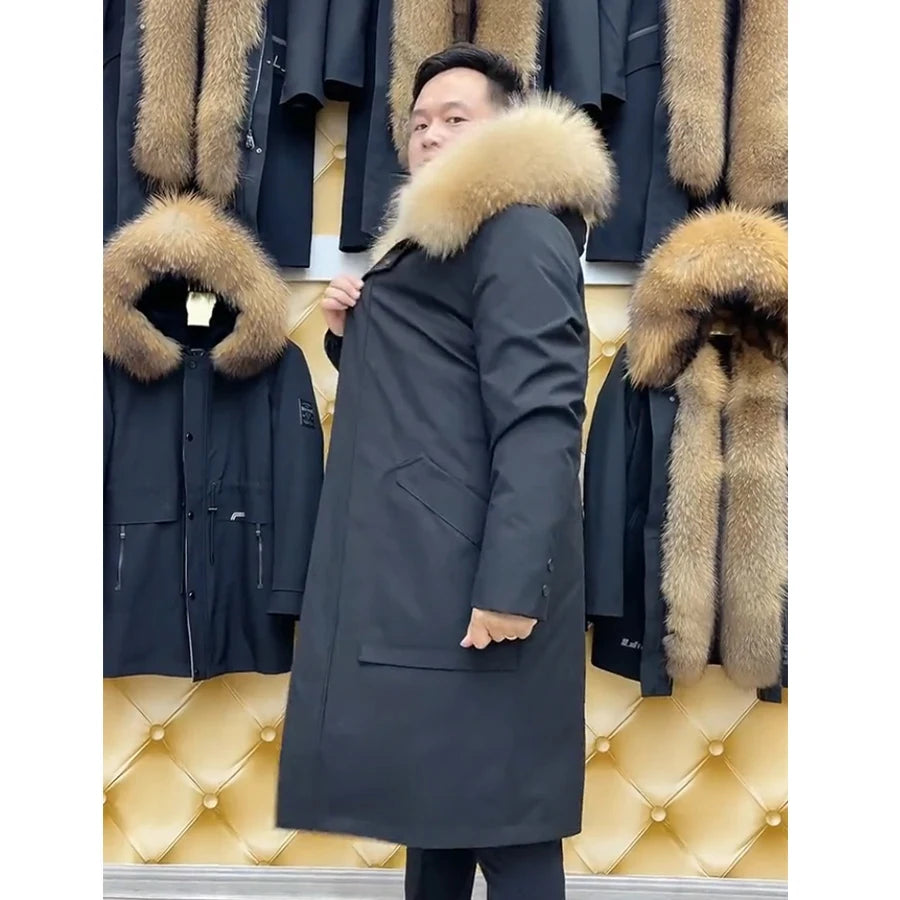A man wearing a long black parka with a large beige fur-trimmed hood, standing in front of a display of other dark parkas with fur collars against a tufted gold wall.