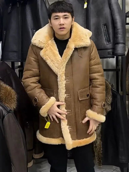 A man wearing a brown shearling-lined jacket with a large beige fur collar, standing in front of a clothing rack filled with black leather jackets.