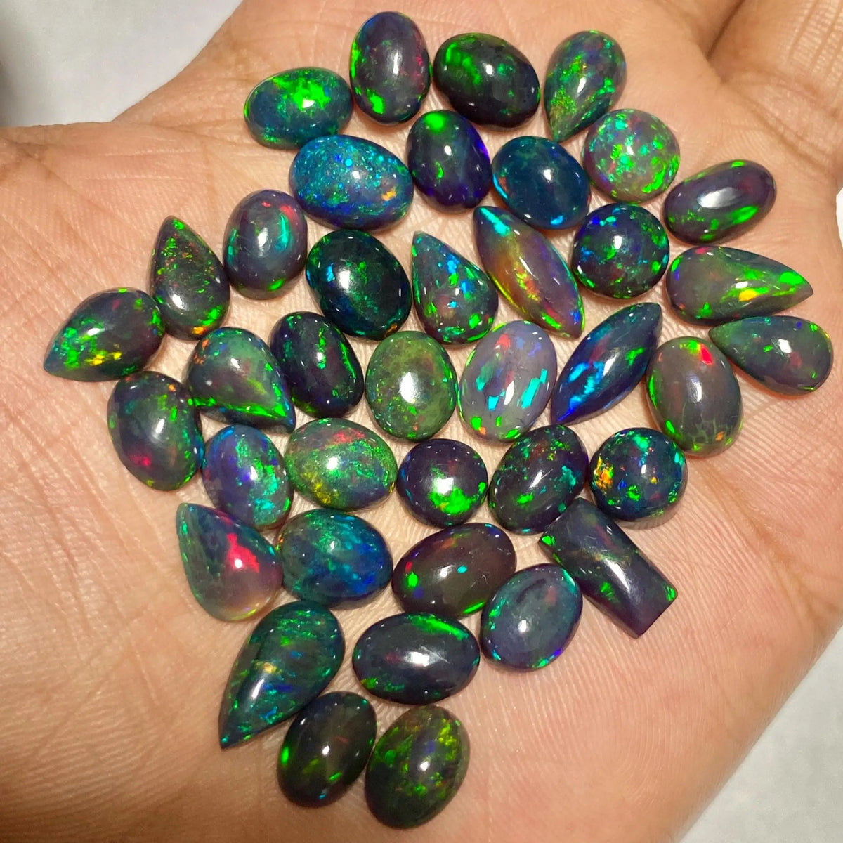 A collection of polished teardrop-shaped opal gemstones with vibrant iridescent flashes of green, blue, pink, and orange, displayed on an open hand.