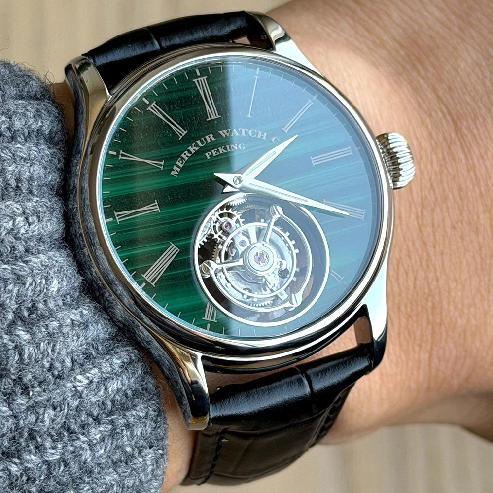 Merkur watch with green face and black leather strap on wrist
