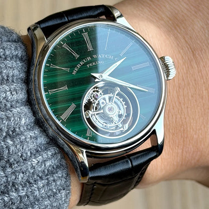 Merkur watch with green face and black leather strap on wrist