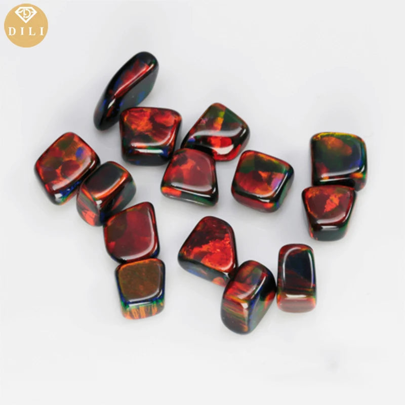 A group of polished tumbled gemstone beads with a rich play-of-color, primarily displaying deep red, black, and hints of orange and green, arranged on a clean white background. A gold circular logo with the brand name 'DILI' is visible in the top-left corner.