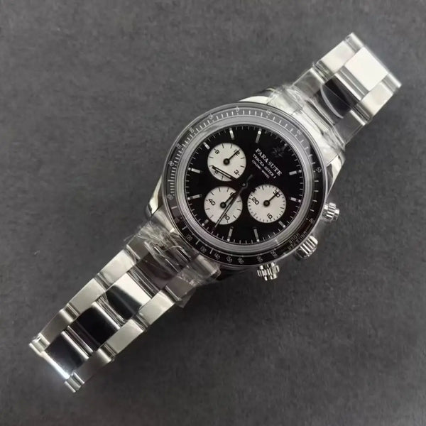 A stainless steel chronograph watch with a black dial and three white subdials, photographed diagonally on a dark gray textured background. The watch is still wrapped in protective plastic.
