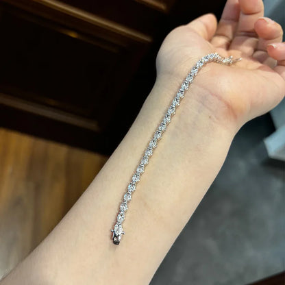 A silver tennis bracelet with clear stones worn on a person's wrist, shown against a dark wooden background.