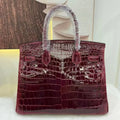 A glossy crocodile-embossed leather handbag in deep burgundy, with protective plastic wrapping on the handles, displayed against a neutral background.