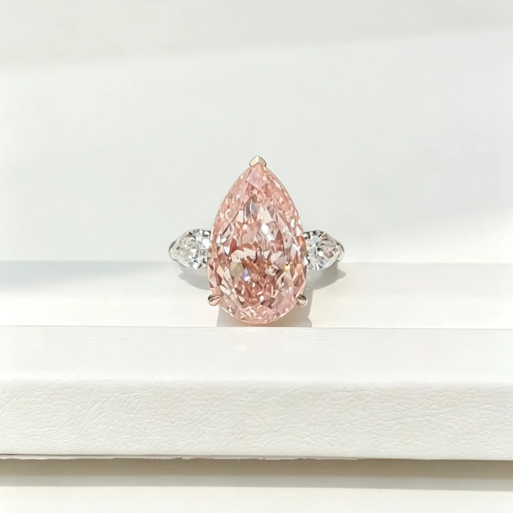 A pear-cut pink diamond ring with a silver-colored band and small side diamonds, displayed on a white surface.