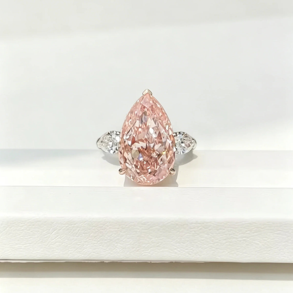 A pear-cut pink diamond ring with a silver-colored band and small side diamonds, displayed on a white surface.