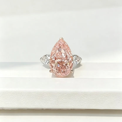 A pear-cut pink diamond ring with a silver-colored band and small side diamonds, displayed on a white surface.