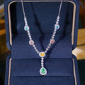 A silver-toned necklace with multiple colorful gemstone accents, displayed inside an open dark blue jewelry box.