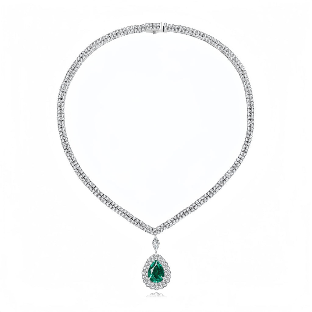 A white gold or platinum tennis necklace featuring a teardrop-shaped green emerald pendant surrounded by a halo of small clear stones, displayed on a clean white background.