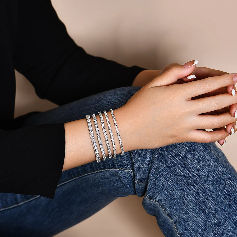 Person wearing multiple diamond bracelets on a neutral background