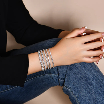 Person wearing multiple diamond bracelets on a neutral background