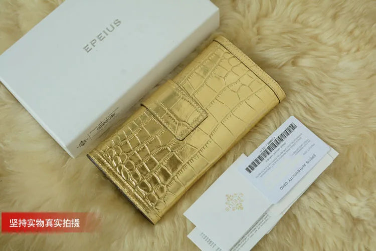 A gold crocodile-embossed wallet or card holder shown with its white EPEIUS box and authenticity card on a beige faux-fur surface.