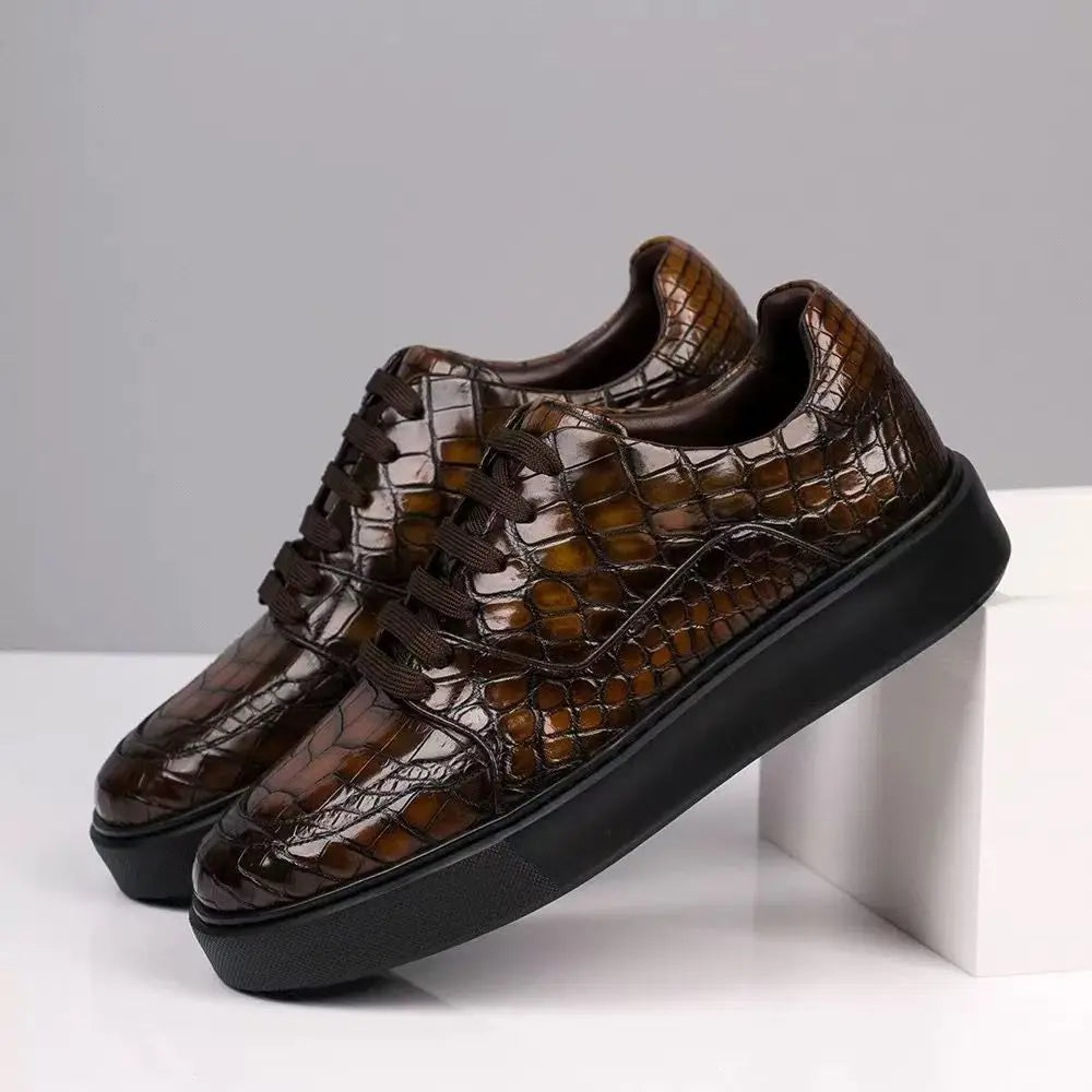 A pair of brown crocodile-embossed leather low-top sneakers with black platform soles, displayed on a white block against a gray background.