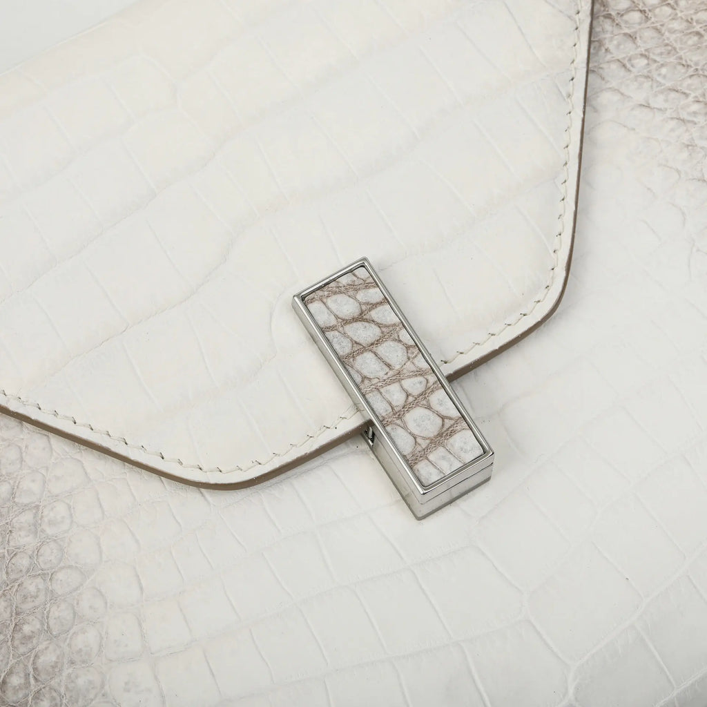 A close-up of a white textured leather clutch bag with a silver-toned metal clasp featuring a white and gray crocodile skin pattern.