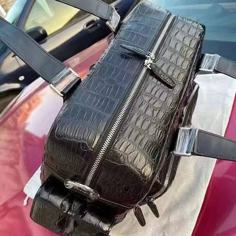 A black crocodile-embossed leather shoulder bag with silver-tone hardware, resting on a white cloth over a red car.
