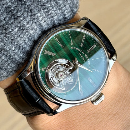Luxury watch with a green and blue face on a wrist, brand 'Merkur' visible