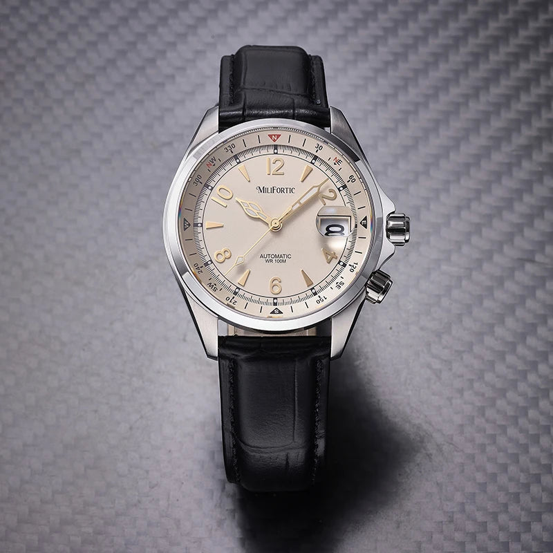 A Milgaforce automatic watch with a silver stainless steel case, a beige dial, and a black leather strap, presented on a textured gray carbon fiber background.