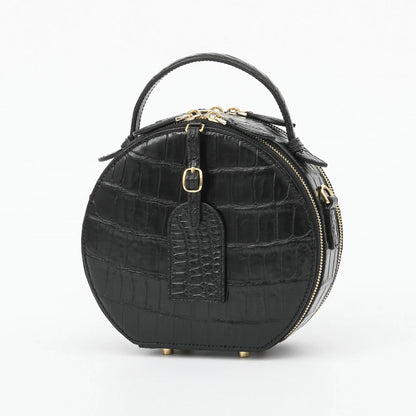 A black crocodile-embossed leather handbag with a top handle, gold-tone hardware, and a front luggage tag, shown on a plain white background.