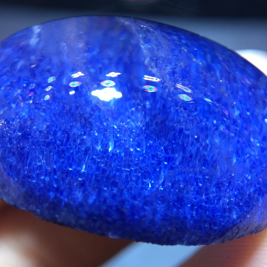 A close-up of a polished deep blue stone or gemstone held in a hand, showing a highly textured, crystalline surface with bright reflective highlights.