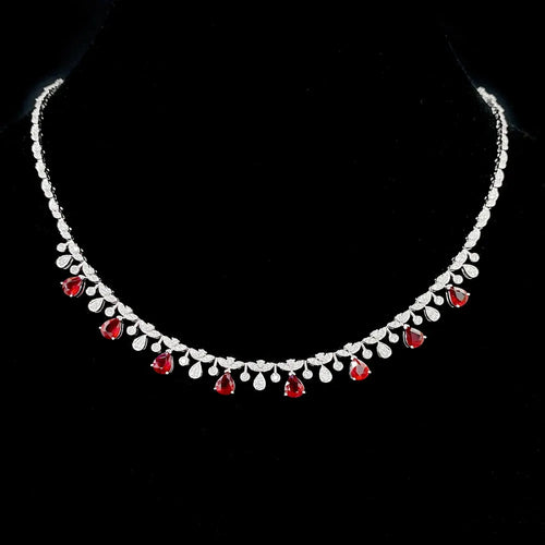 A silver-toned necklace with a row of clear teardrop-shaped stones and alternating red teardrop gemstones, displayed on a black background.