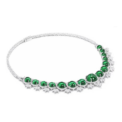 A silver-toned tennis necklace featuring a row of oval-cut emerald green gemstones and small clear stones, displayed on a clean white background.