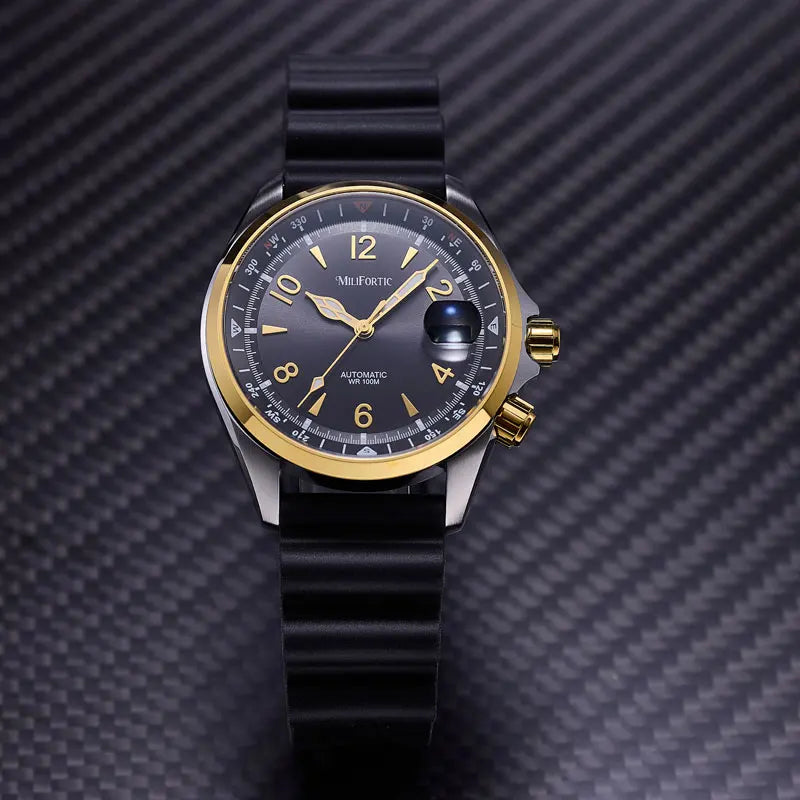 A Mil-Fort wristwatch with a black rubber strap, black dial, and gold-tone bezel and hands, photographed against a dark carbon-fiber-textured background.