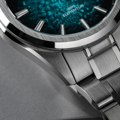 Close-up of a stainless steel watch with a textured teal-blue dial and matching metal bracelet, showing the brand text 'ELEMENTUM' on the face.