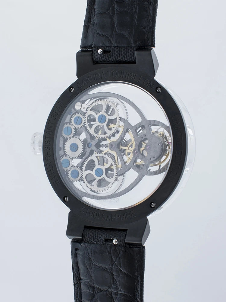 A close-up of a skeleton watch showing a detailed mechanical movement with silver gears and blue accents, housed in a black case with a black textured strap, on a light gray background.