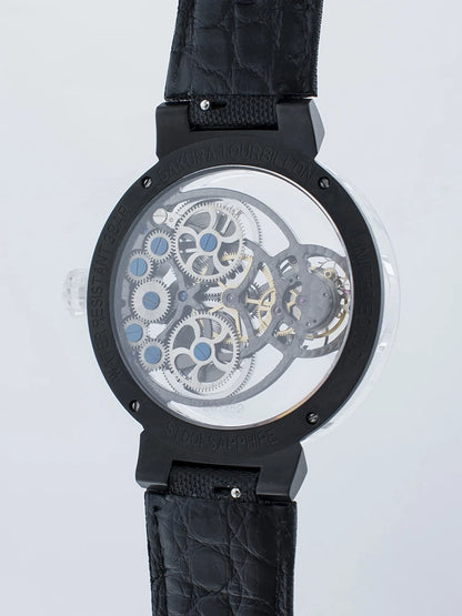 A close-up of a skeleton watch showing a detailed mechanical movement with silver gears and blue accents, housed in a black case with a black textured strap, on a light gray background.