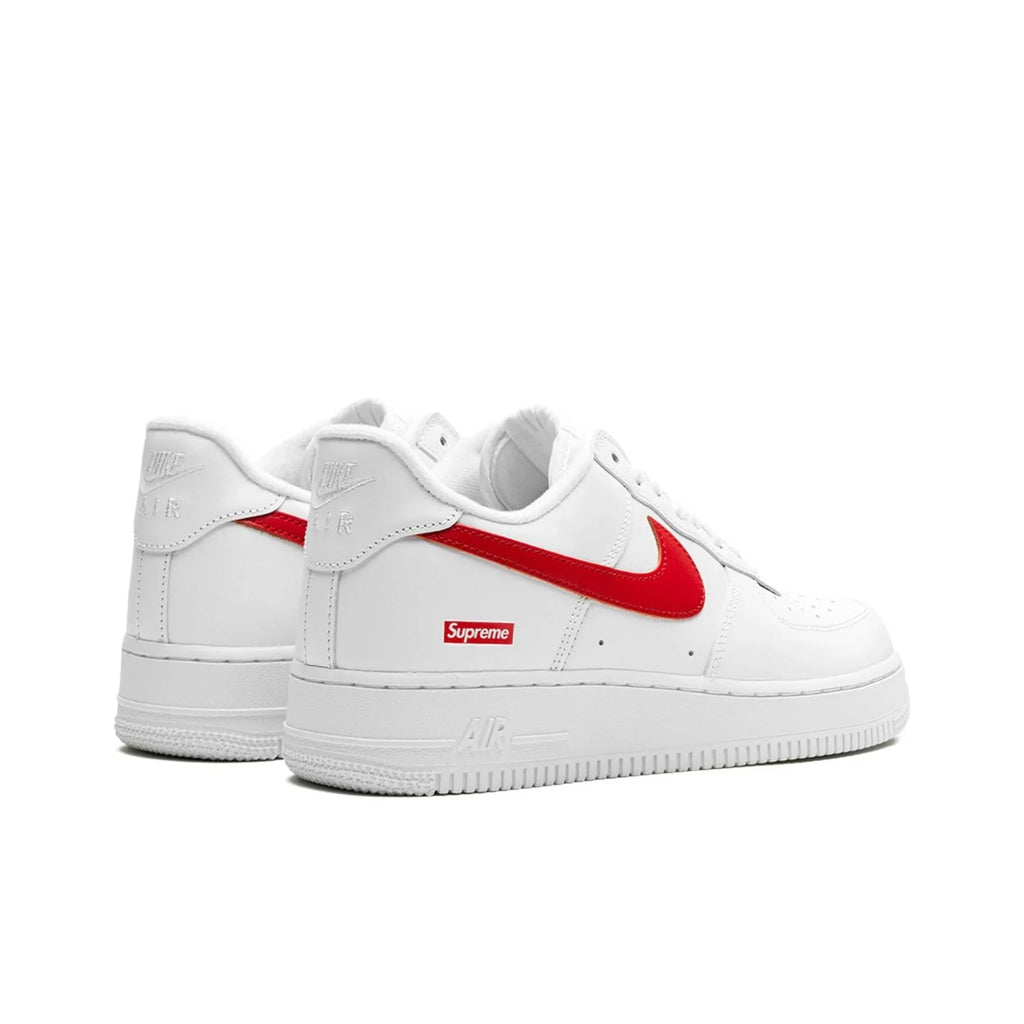 White Nike Air Force 1 Low sneakers with a red Supreme Swoosh and a red Supreme box logo on the side, shown against a plain white background.