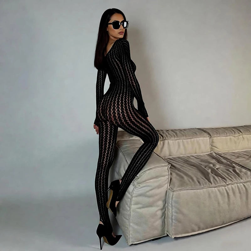 Woman in a black patterned outfit standing on a beige sofa against a gray background