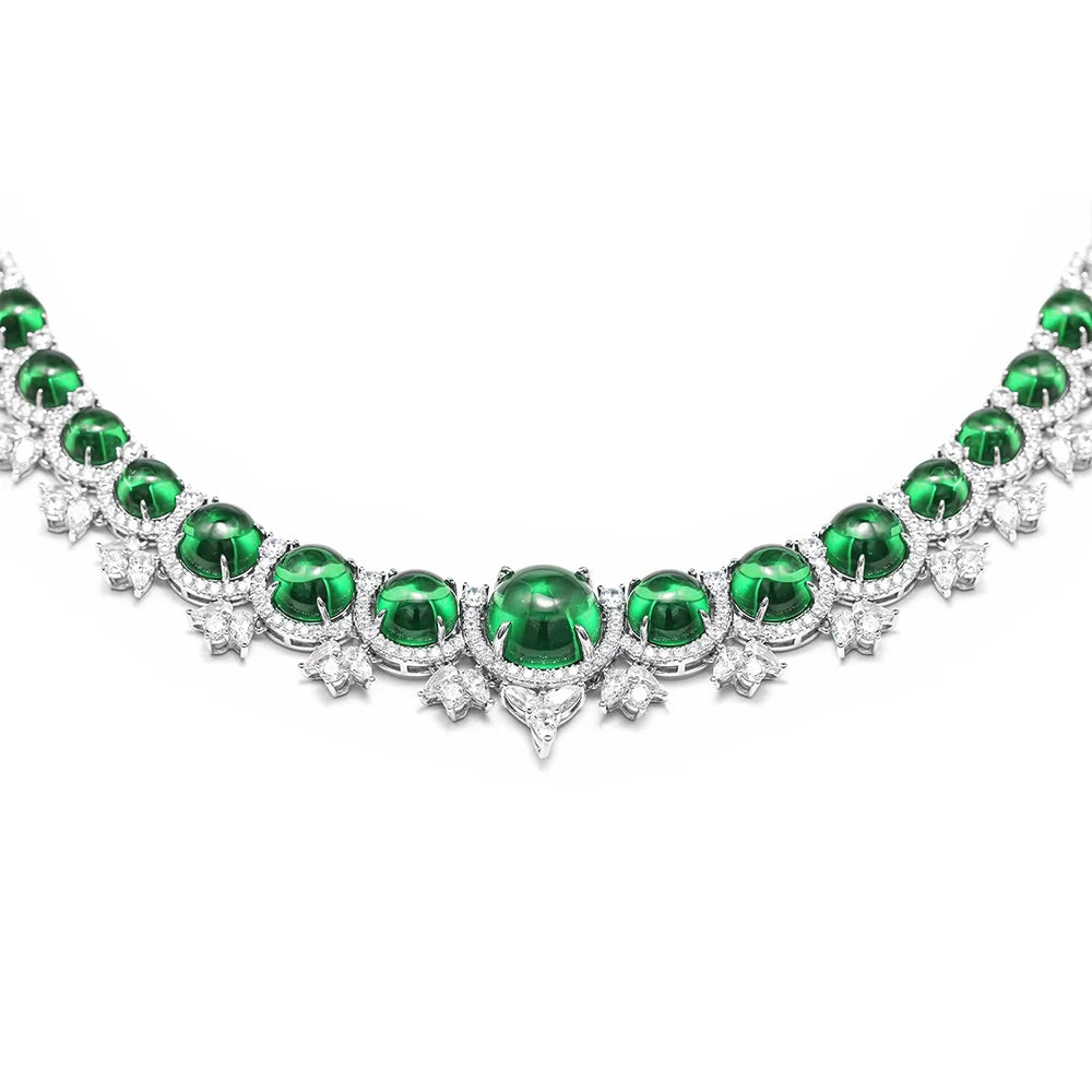 A silver-toned necklace featuring a row of oval-cut emerald green gemstones, each surrounded by small clear stones in starburst and round settings, photographed on a plain white background.